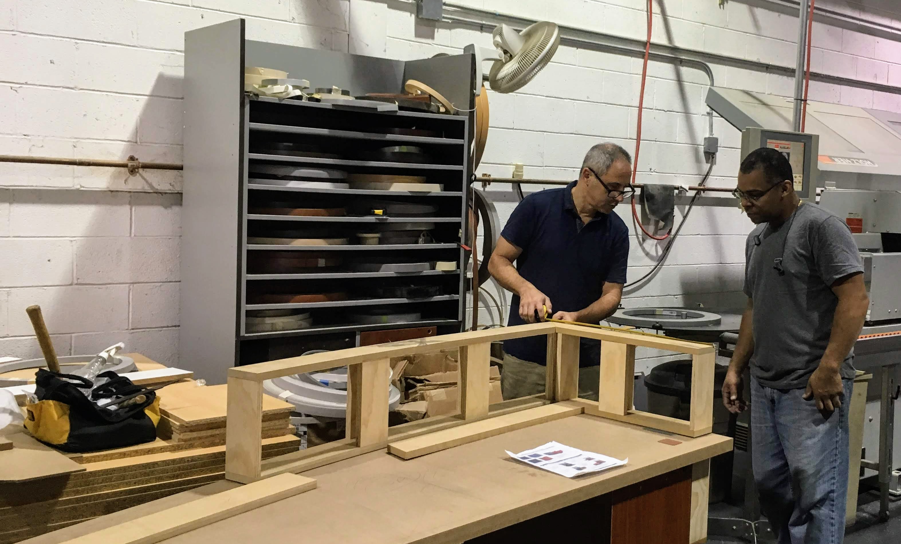 Two men discussing something while measuring a wood for a furniture